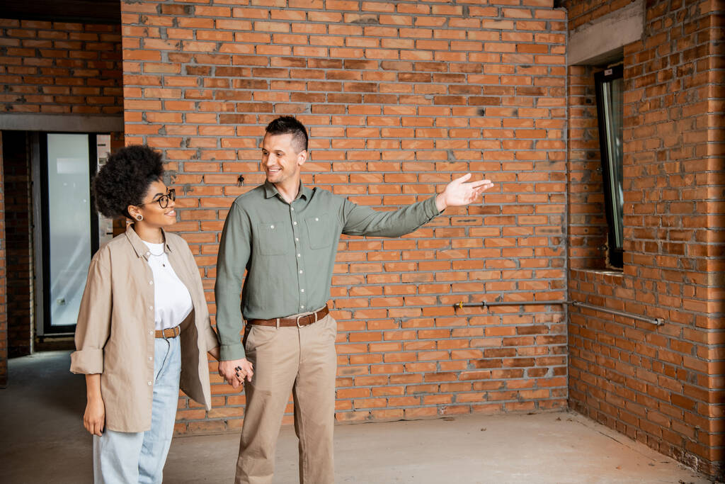 hombre feliz señalando con la mano mientras que muestra nueva casa a la mujer afroamericana - Foto, imagen