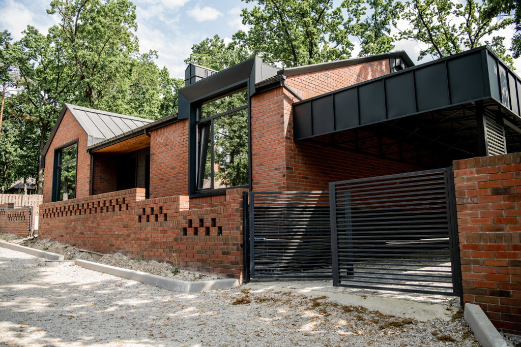 woontrends, bakstenen eigentijds huis met metalen poorten en stenen hek - Foto, afbeelding