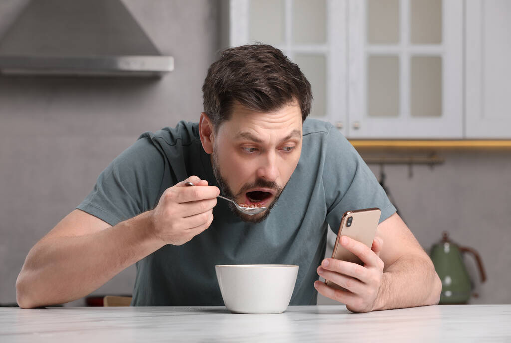 Man using smartphone while having breakfast at table in kitchen. Internet addiction - Photo, Image