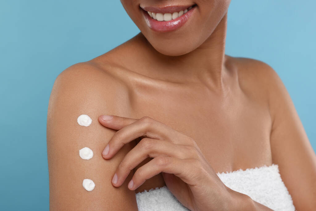 jonge vrouw aanbrengen lichaam crème op arm op licht blauwe achtergrond, close-up - Foto, afbeelding