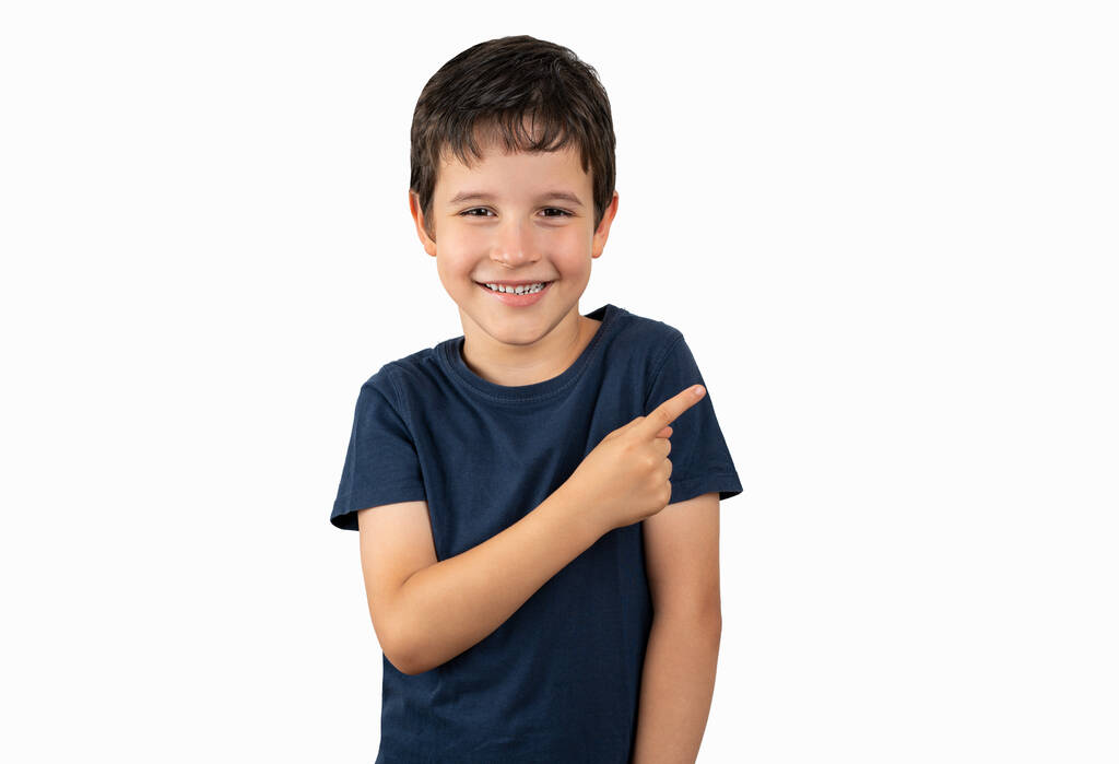 Niño pequeño sobre fondo aislado sonriendo y mirando a la cámara apuntando con una mano y los dedos hacia un lado. - Foto, imagen