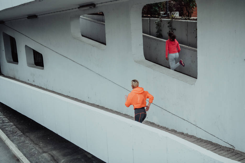 Dos mujeres en ropa deportiva corriendo en un entorno urbano moderno. El concepto de un estilo de vida deportivo y saludable.  - Foto, imagen