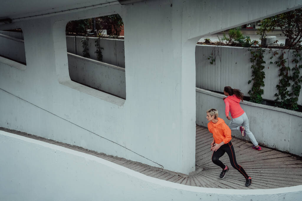 Twee vrouwen in sportkleding in een moderne stedelijke omgeving. Het concept van een sportieve en gezonde levensstijl.  - Foto, afbeelding