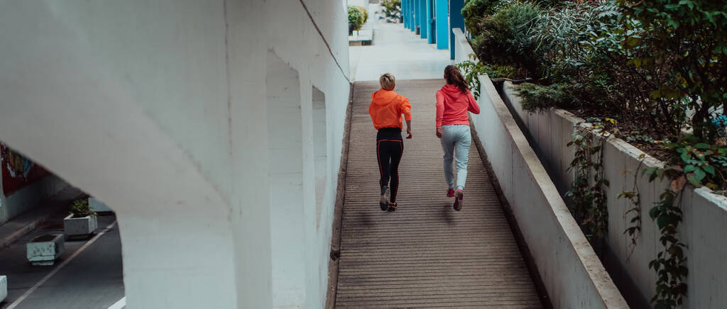 Two women in sports clothes running in a modern urban environment. The concept of a sporty and healthy lifestyle.  - Photo, image