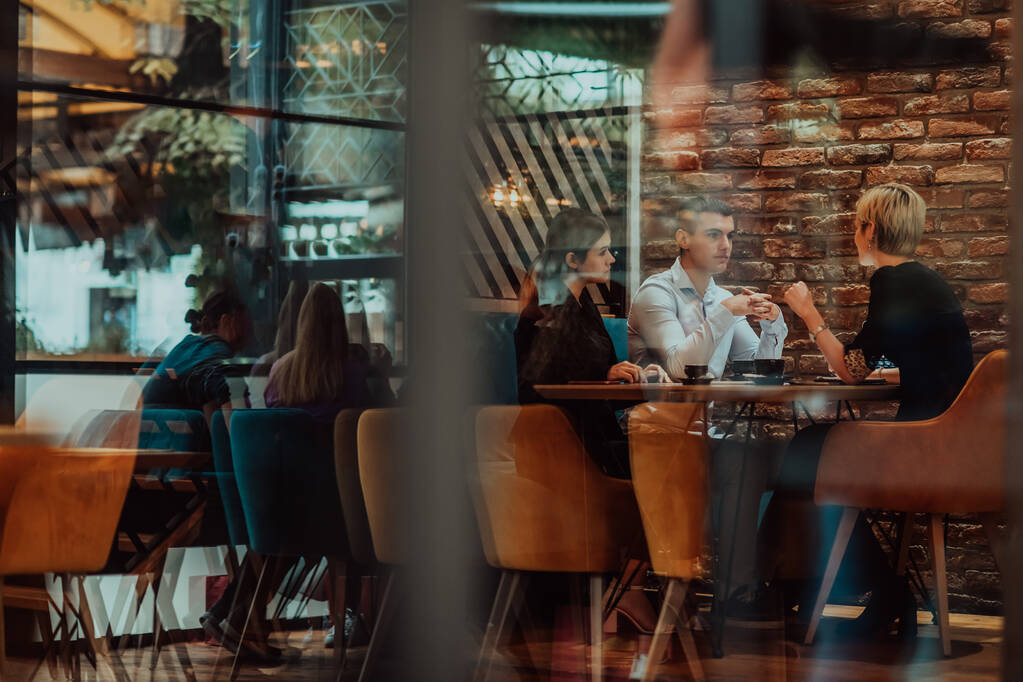 Photo through the glass of a group of business people sitting in a cafe and discussing business plans and ideas for new online commercial services.  - Fotoğraf, Görsel