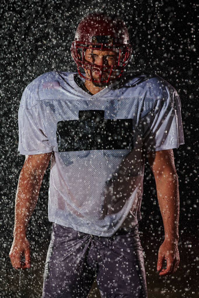 Amerikan Futbol Sahası: Yalnız Atletizm Savaşçısı Kask Tutuyor ve Oynamaya Hazır. Oyuncu koşmaya, saldırmaya ve sayı yapmaya hazırlanıyor. Dramatik Sisli Yağmurlu Gece, Mavi Işık. - Fotoğraf, Görsel