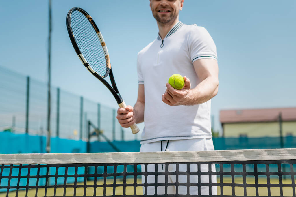 cropped view of man in sportswear holding tennis racquet and ball near net, player, hobby and sport - Photo, Image