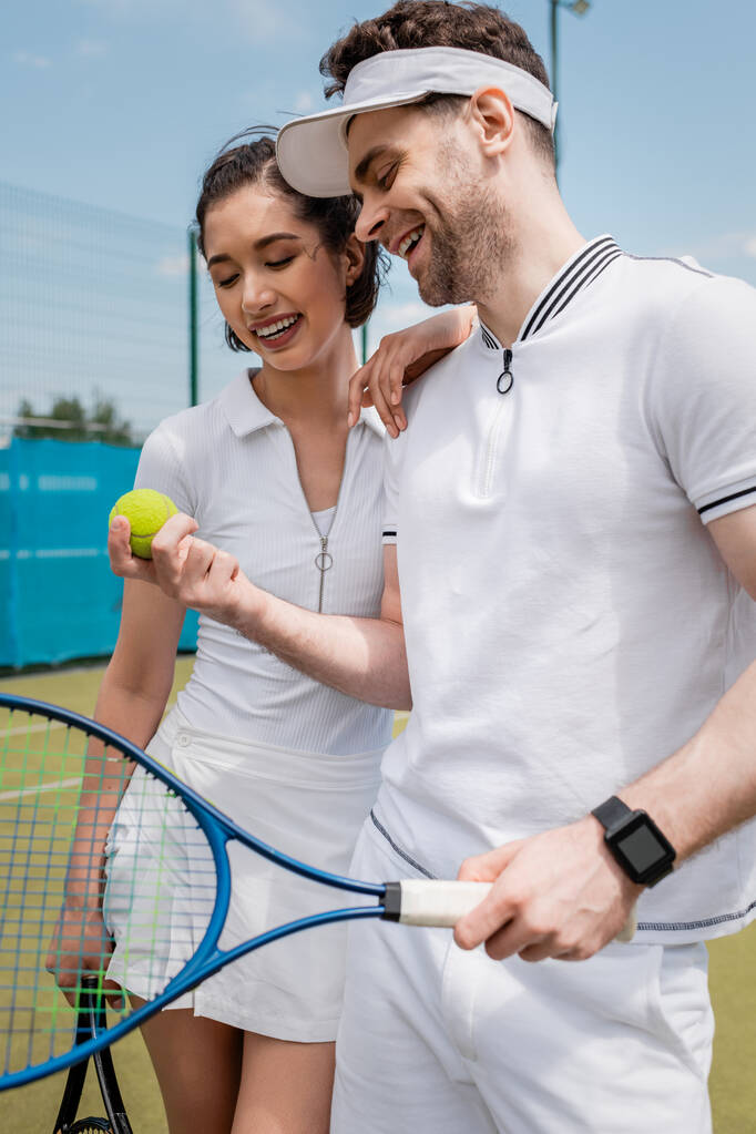 コート,レジャー,スポーツ,夏の楽しみでテニスボールを見ているアクティブな着用で陽気なカップル - 写真・画像