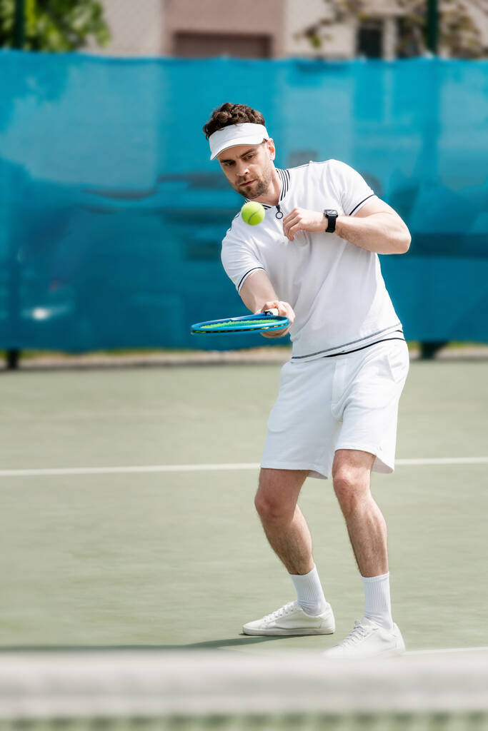 Zıplayan tenis topu, sahada pratik yapan yakışıklı bir tenisçi, raket, spor ve eğlence tutuyor. - Fotoğraf, Görsel