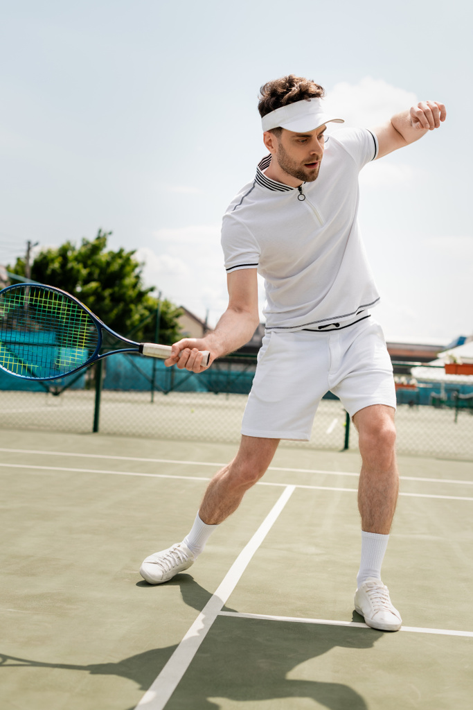 спортсмен в спортивном козырьке, держит ракетку и играет в теннис на корте, тренируется и мотивируется - Фото, изображение