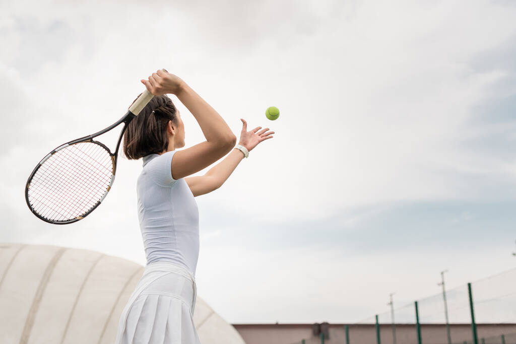 πίσω όψη του γυναικείου παίκτη χτύπημα της μπάλας, ενώ παίζει τένις στο γήπεδο, κίνητρο και τον αθλητισμό - Φωτογραφία, εικόνα