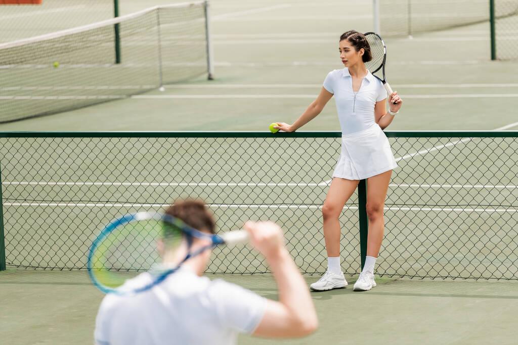 Tennisspielerin steht in Netznähe und hält Schläger in der Hand, Mann in aktiver Kleidung auf verschwommenem Vordergrund - Foto, Bild