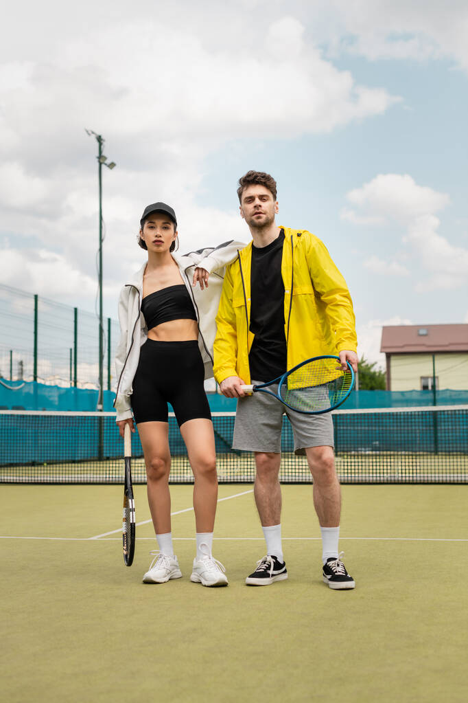 mies ja nainen tyylikäs aktiivinen kulumista seisoo kentällä tennismailat, terveiden elämäntapojen, urheilu - Valokuva, kuva