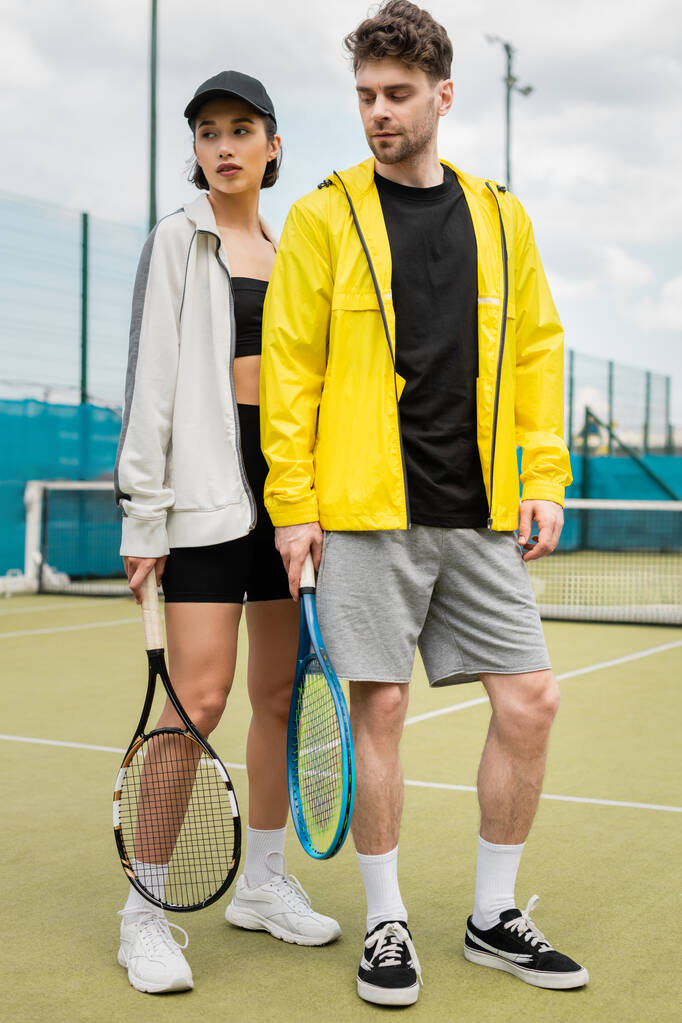 sport, modieus koppel op tennisbaan met rackets, man en vrouw in stijlvolle outfits - Foto, afbeelding