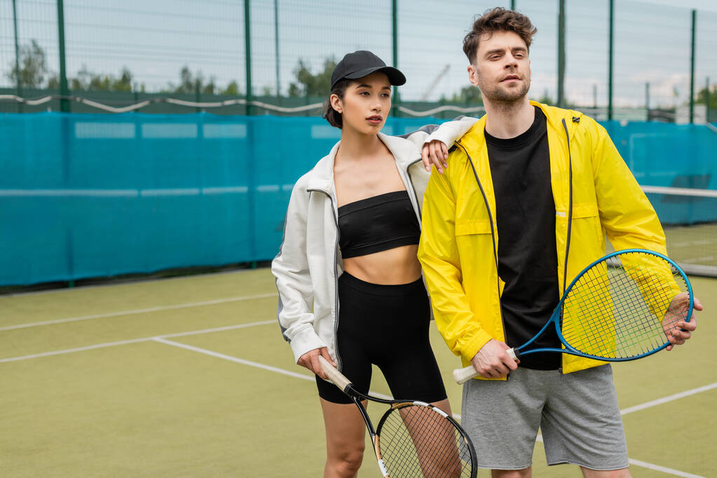 sport, fashionable couple standing on court with tennis racquets, man and woman in stylish outfits - Photo, Image