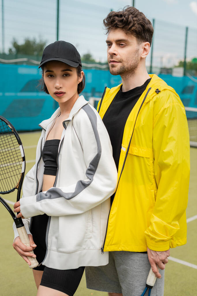 sport, uomo e donna alla moda in piedi sul campo con racchetta da tennis, coppia sportiva, hobby - Foto, immagini