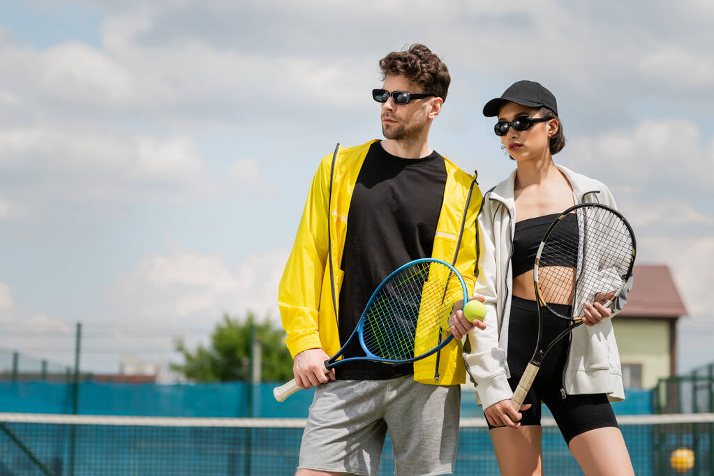 letní sport, muž a žena ve slunečních brýlích stojící na tenisovém kurtu s raketami, sportovci módní - Fotografie, Obrázek