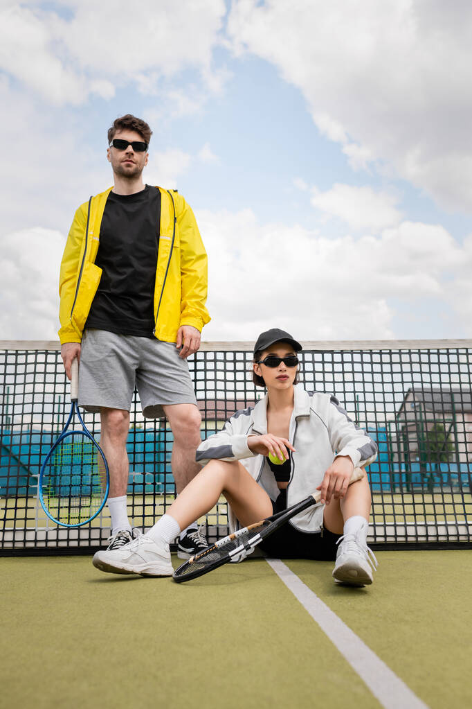 пара спорт, чоловік і жінка в сонцезахисних окулярах позують на тенісному корті з ракетками, спортсмени моди - Фото, зображення