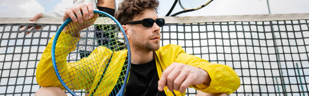 pancarta, hombre en gafas de sol y ropa activa celebración raqueta cerca de la mujer y la red de tenis, moda deportiva - Foto, imagen