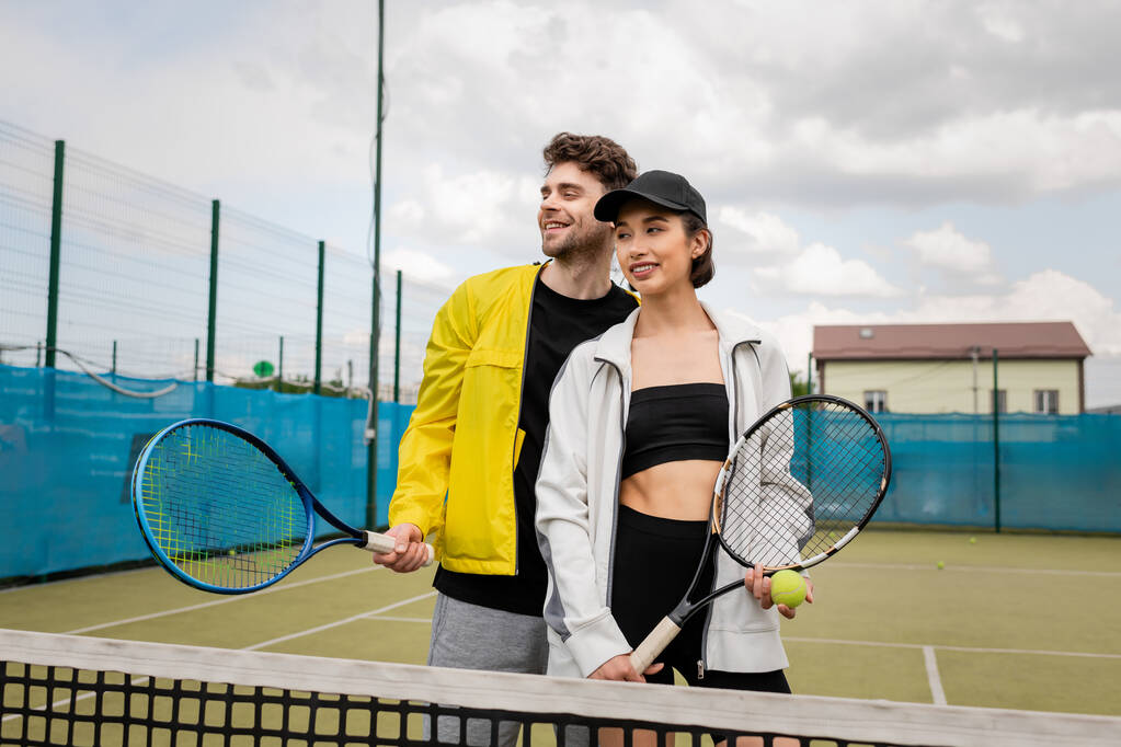 boldog férfi és nő aktív kopás gazdaság ütők közelében net teniszpálya, életmód, mosoly - Fotó, kép