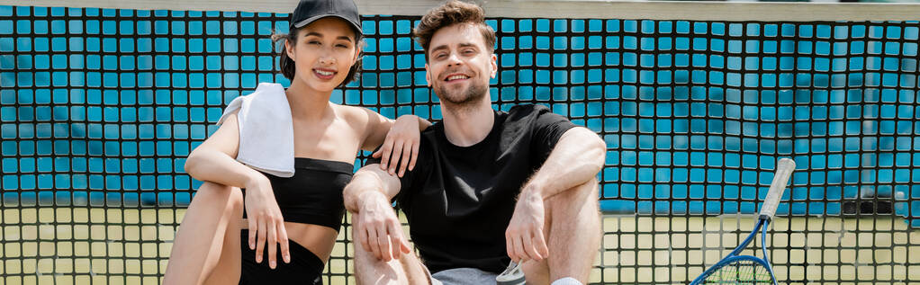 banner, healthy lifestyle, happy man and woman in active wear resting near tennis net on court - Photo, Image