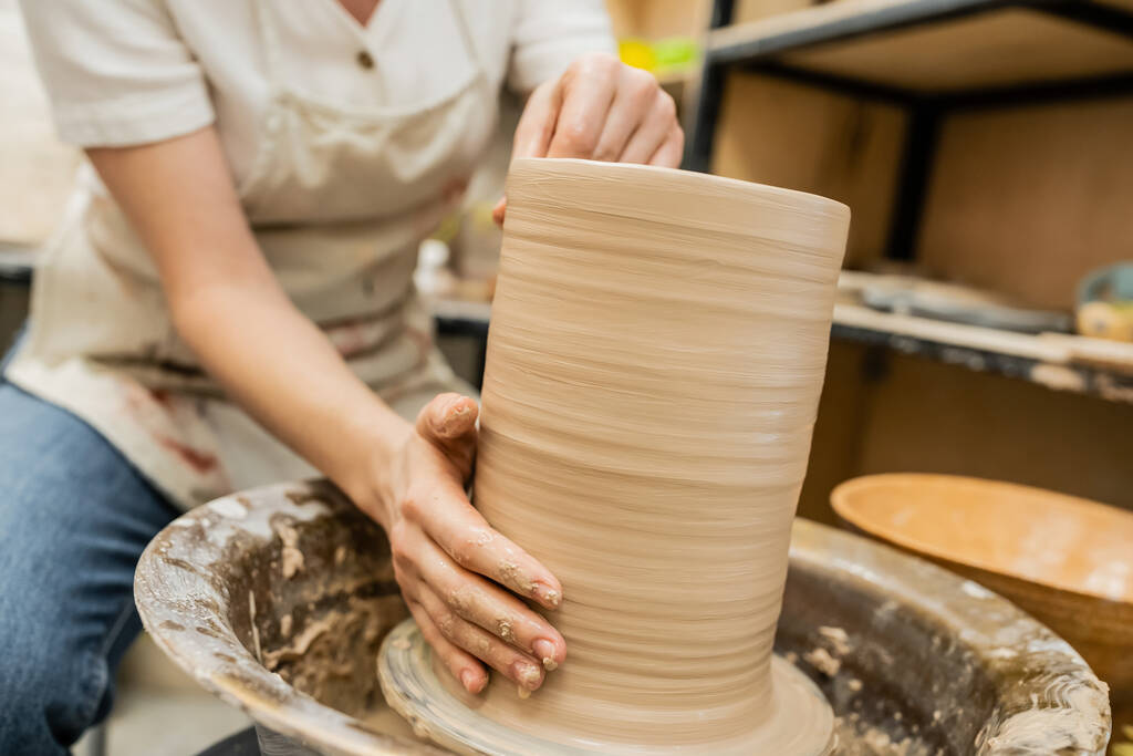 Önlüklü bulanık kadın, atölyede çömlek çarkında kil vazo yaratıyor. - Fotoğraf, Görsel
