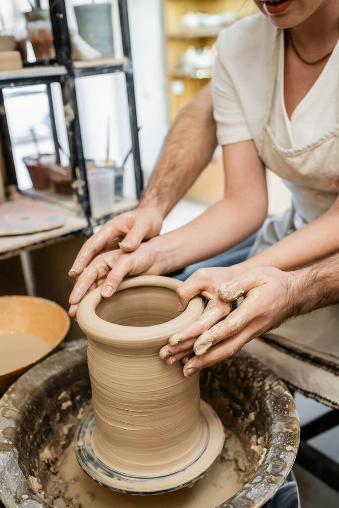Gesneden weergave van pottenbakker gieten klei met vriendin op aardewerk wiel in keramische werkplaats - Foto, afbeelding