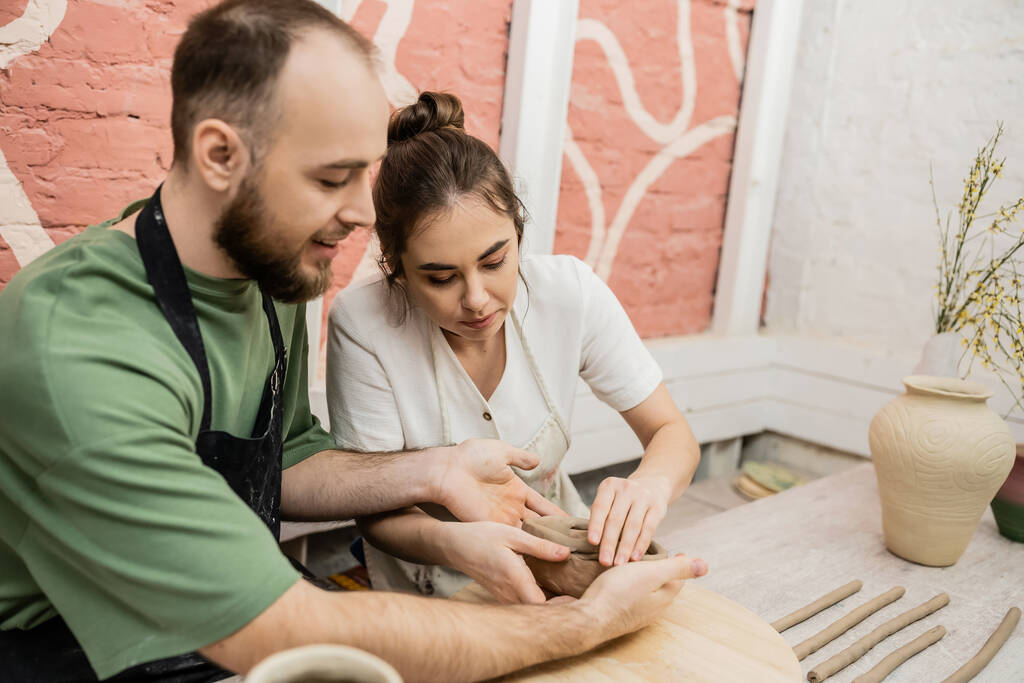 Романтическая пара ремесленников в фартуках, формирующих глиняную посуду в керамической мастерской - Фото, изображение