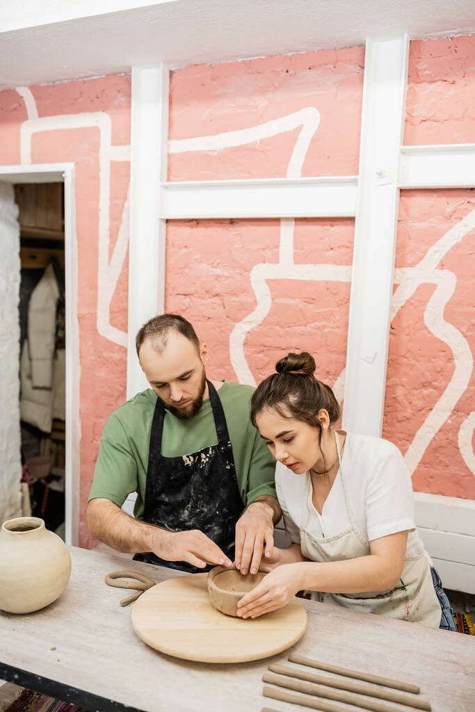 Pareja de escultores moldeando tazón de arcilla mientras trabajan juntos en taller de cerámica - Foto, imagen