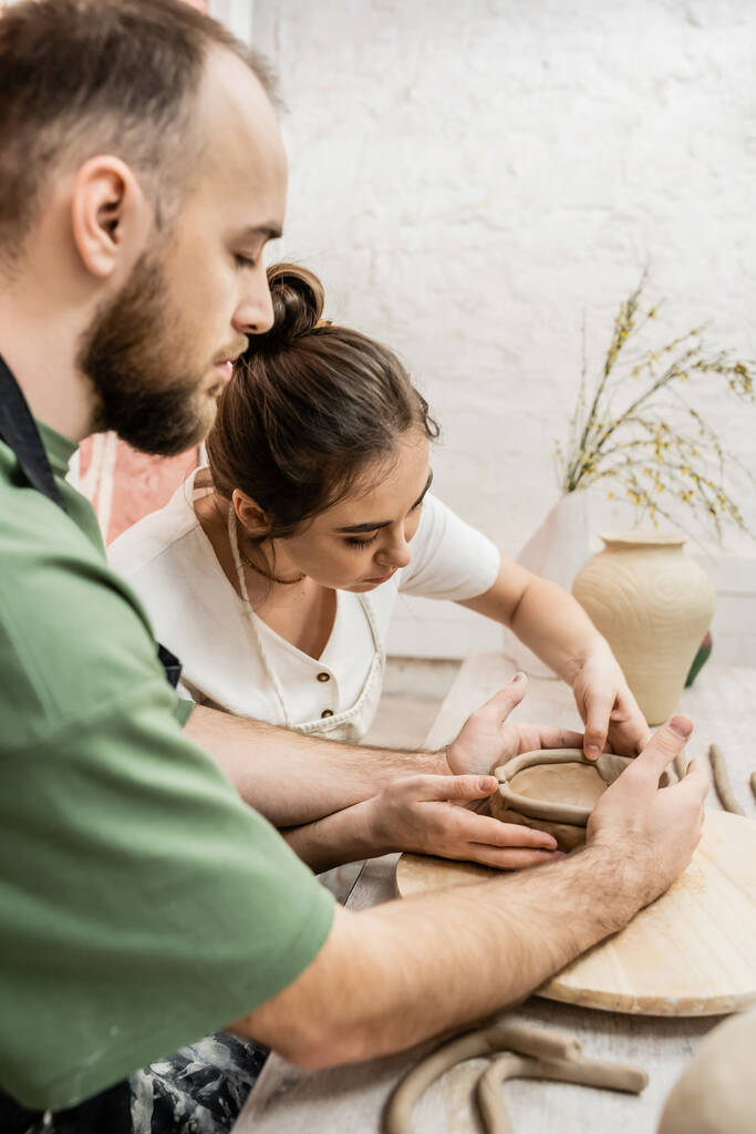 Handwerkerin in Schürze formt mit Freund Tonschale in Keramik-Werkstatt - Foto, Bild