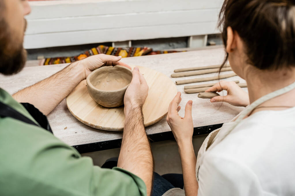 Vue recadrée de l'artisan en tablier façonnant bol d'argile près de petite amie dans l'atelier de poterie - Photo, image