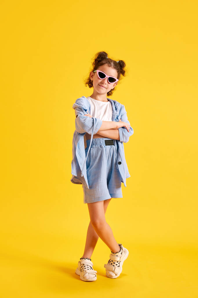 Retrato completo de menina elegante, criança em óculos de sol posando contra o fundo do estúdio amarelo. Vibe de verão. Conceito de emoções, infância, educação, moda, estilo de vida, anúncio - Foto, Imagem