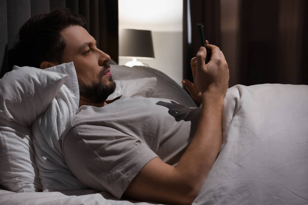 Чоловік використовує смартфон у ліжку вночі. Інтернет залежність
 - Фото, зображення