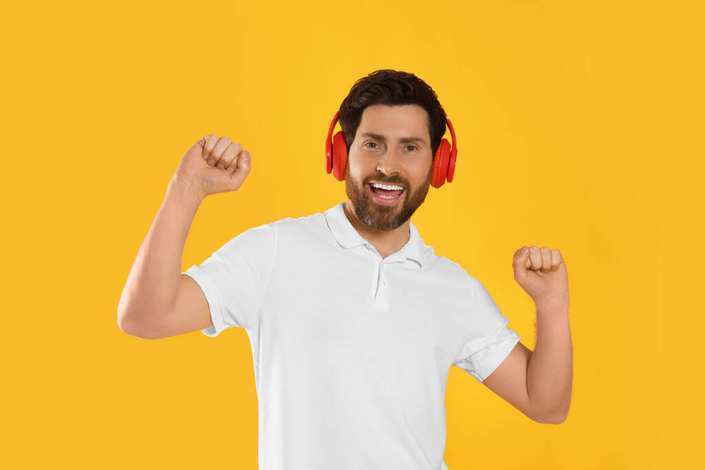 Hombre feliz escuchando música con auriculares sobre fondo amarillo - Foto, imagen