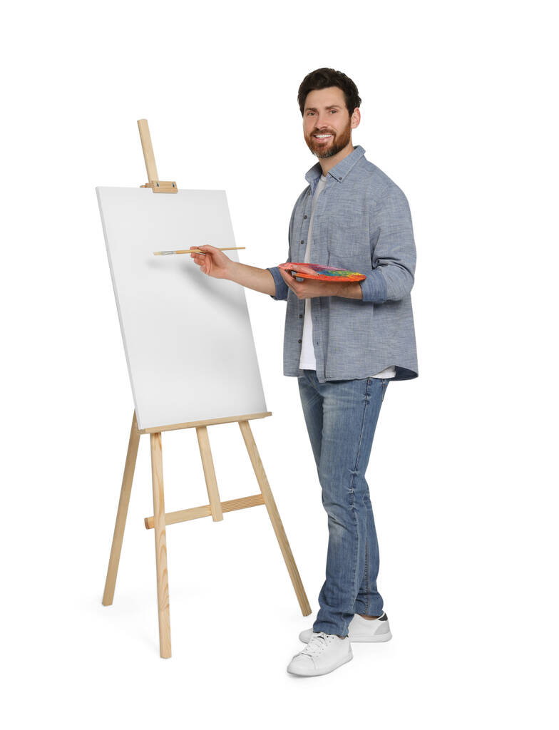 白を背景に筆で絵を描く幸せな男。キャンバスを保持するためにイーゼルを使用 - 写真・画像