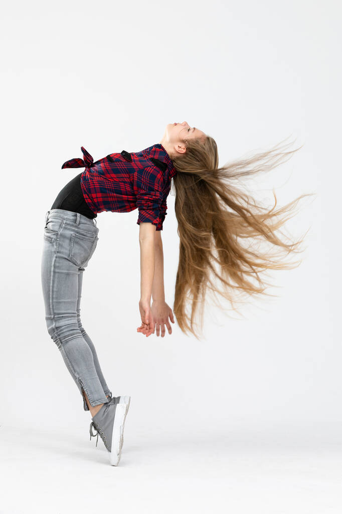 Das Mädchen trägt taillierte Jeans, kariertes Hemd und Sportschuhe. Die junge Frau posiert für das Foto und vollführt eine schwierige Akrobatik, indem sie auf Zehenspitzen steht und ihren Rücken wölbt. Die Haare der Mädchen können - Foto, Bild