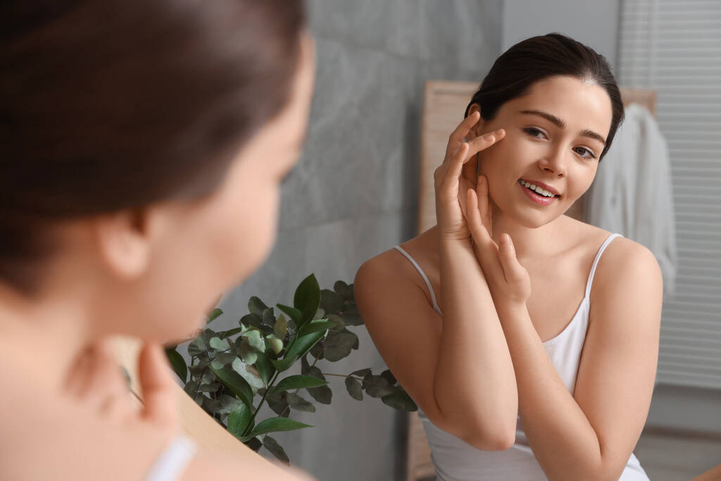 jonge vrouw masseren haar gezicht in de buurt spiegel in badkamer - Foto, afbeelding