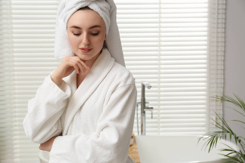 Beautiful woman wearing white robe in bathroom, space for text - Photo, Image