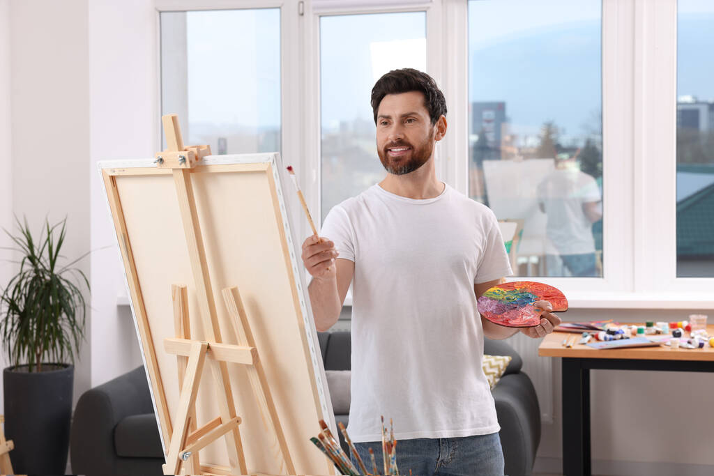 Hombre pintando en el estudio. Usando caballete para sostener el lienzo - Foto, imagen