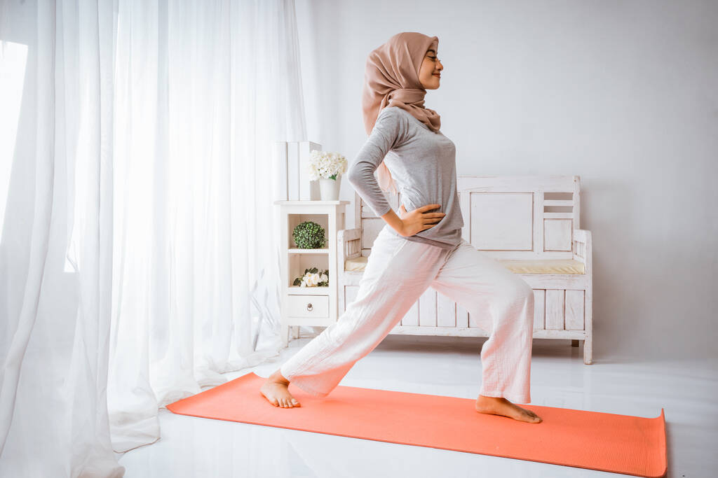 Müslüman kadın egzersiz öncesi ısınıyor. Turuncu şiltede gülümseyen bir odada egzersiz yapıyor. - Fotoğraf, Görsel