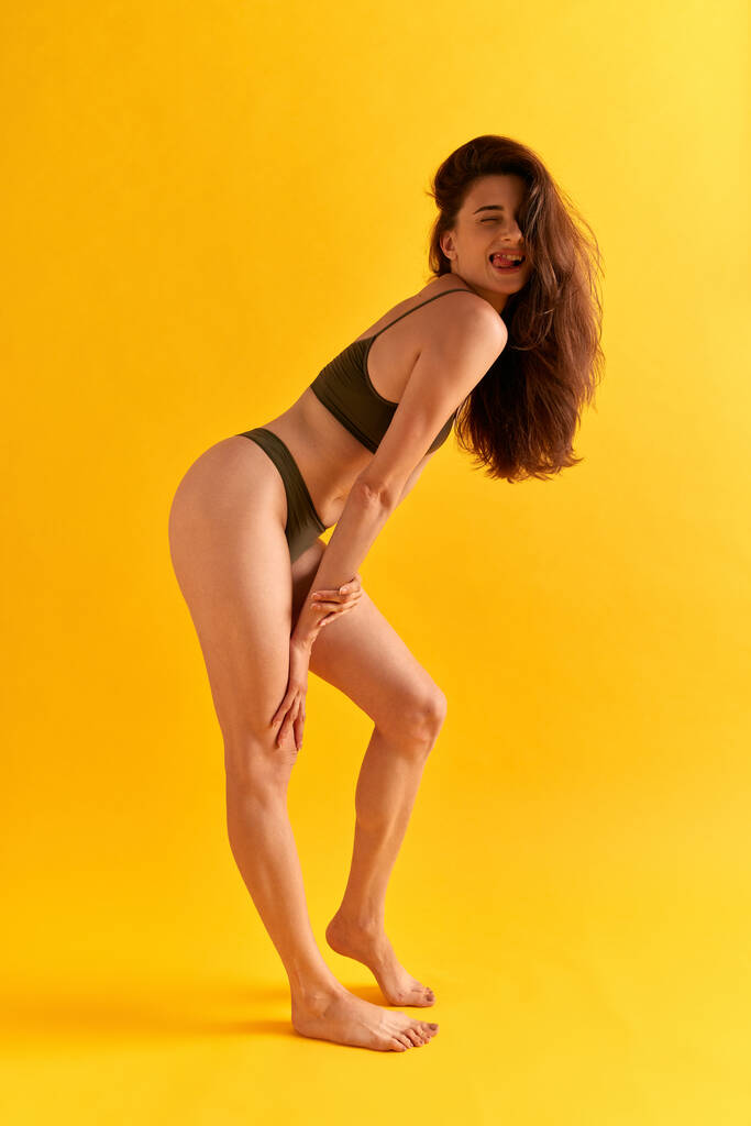 Ganzkörperporträt einer positiven jungen Frau mit schlankem Körper, schlanken Beinen, die in Unterwäsche vor gelbem Studiohintergrund sitzt. Konzept weiblicher Schönheit, Körperpflege, Fitness, Sport, Gesundheit, Figur, Werbung - Foto, Bild