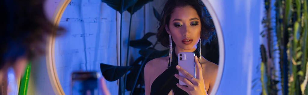 moda joven asiático mujer tomando selfie en smartphone cerca espejo y plantas en night club, banner - Foto, imagen
