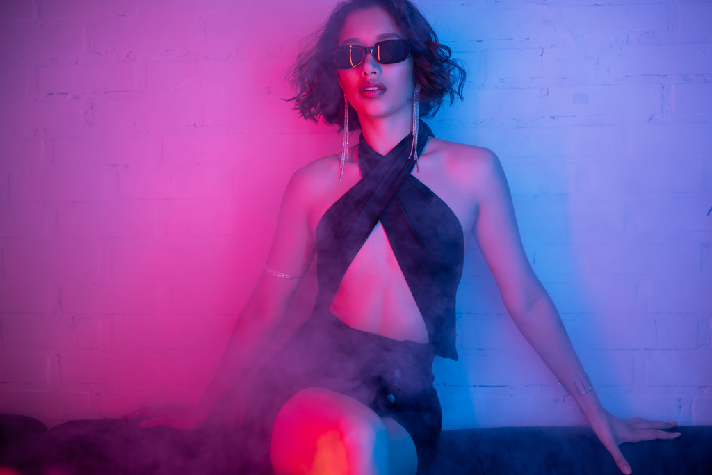 elegante ásia mulher no sexy vestido e óculos de sol posando no fumaça e néon luz no noite clube - Foto, Imagem