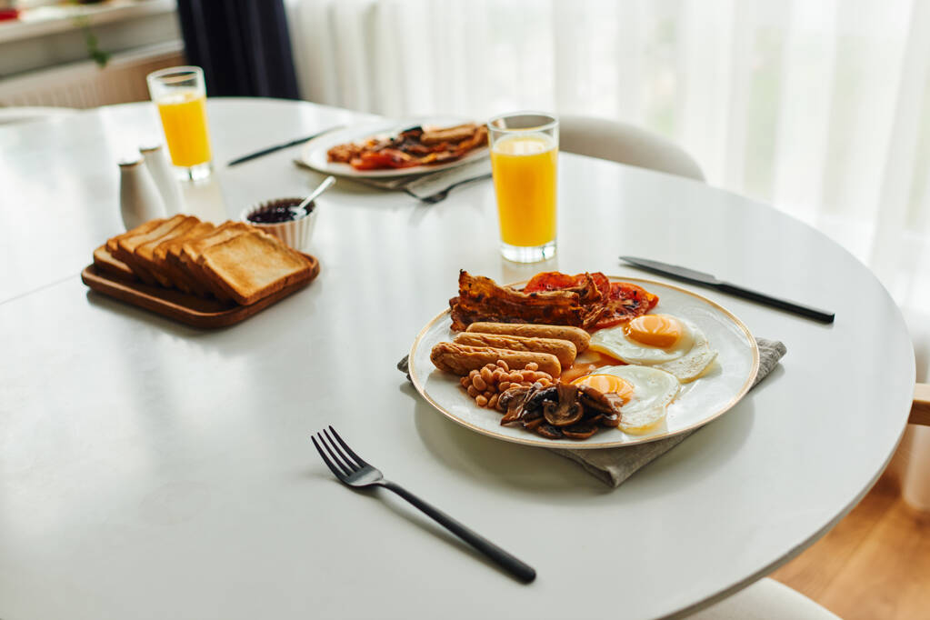 Smaczne śniadanie z fasolą i smażonymi jajkami na stole w pobliżu sztućców i soku pomarańczowego w domu - Zdjęcie, obraz