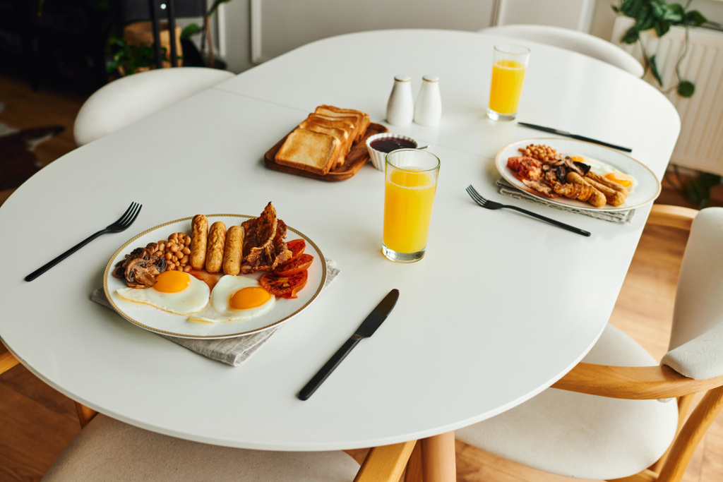 Colazione gustosa con uova fritte vicino ai toast e succo d'arancia sul tavolo a casa al mattino - Foto, immagini