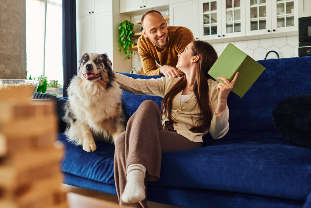 Mosolygó pár időt tölt könyv és a határ collie kutya kanapén közelében popcorn a nappaliban - Fotó, kép
