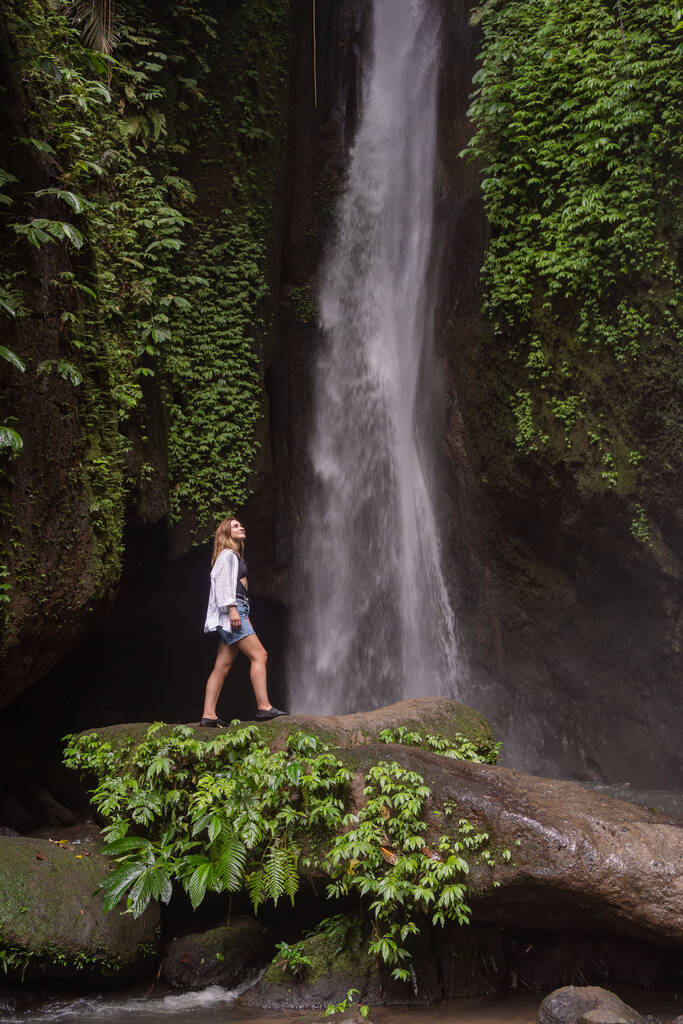 Utazási életmód. Fiatal utazó nő a trópusi erdő vízesésénél. Leke Leke vízesés, Bali, Indonézia - Fotó, kép