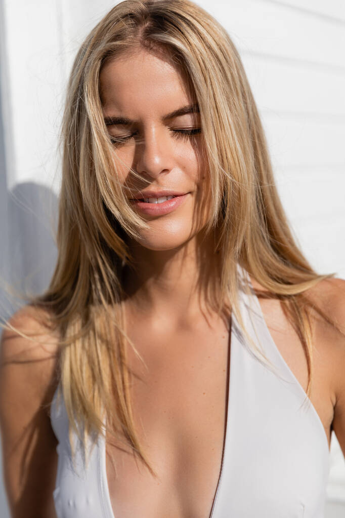 Een prachtige blonde vrouw in een witte top slaat een pose op een zonnige dag in Miami Beach. - Foto, afbeelding