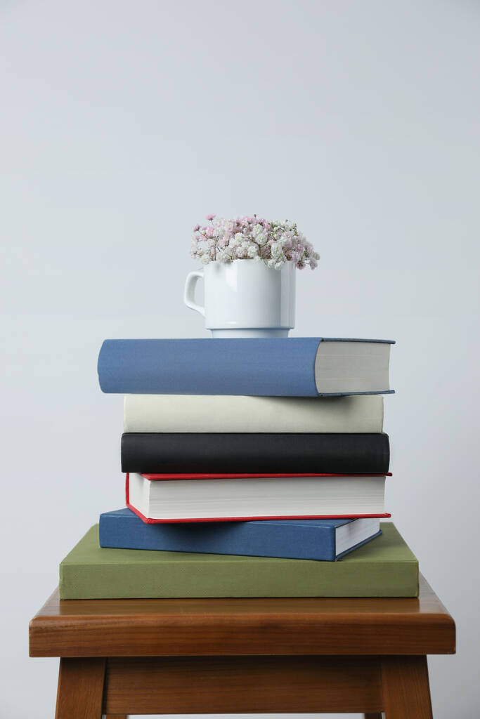 Hardcover books and cup with flowers on wooden stool near white wall - Photo, Image