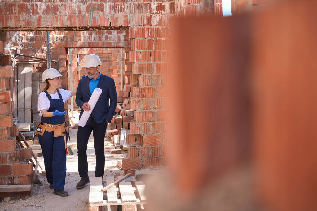 Дружня жінка головний будівельник вітає головного архітектора з відбитками і показує прогрес будівництва, інвестора або інспектора наглядового будинку всередині - Фото, зображення